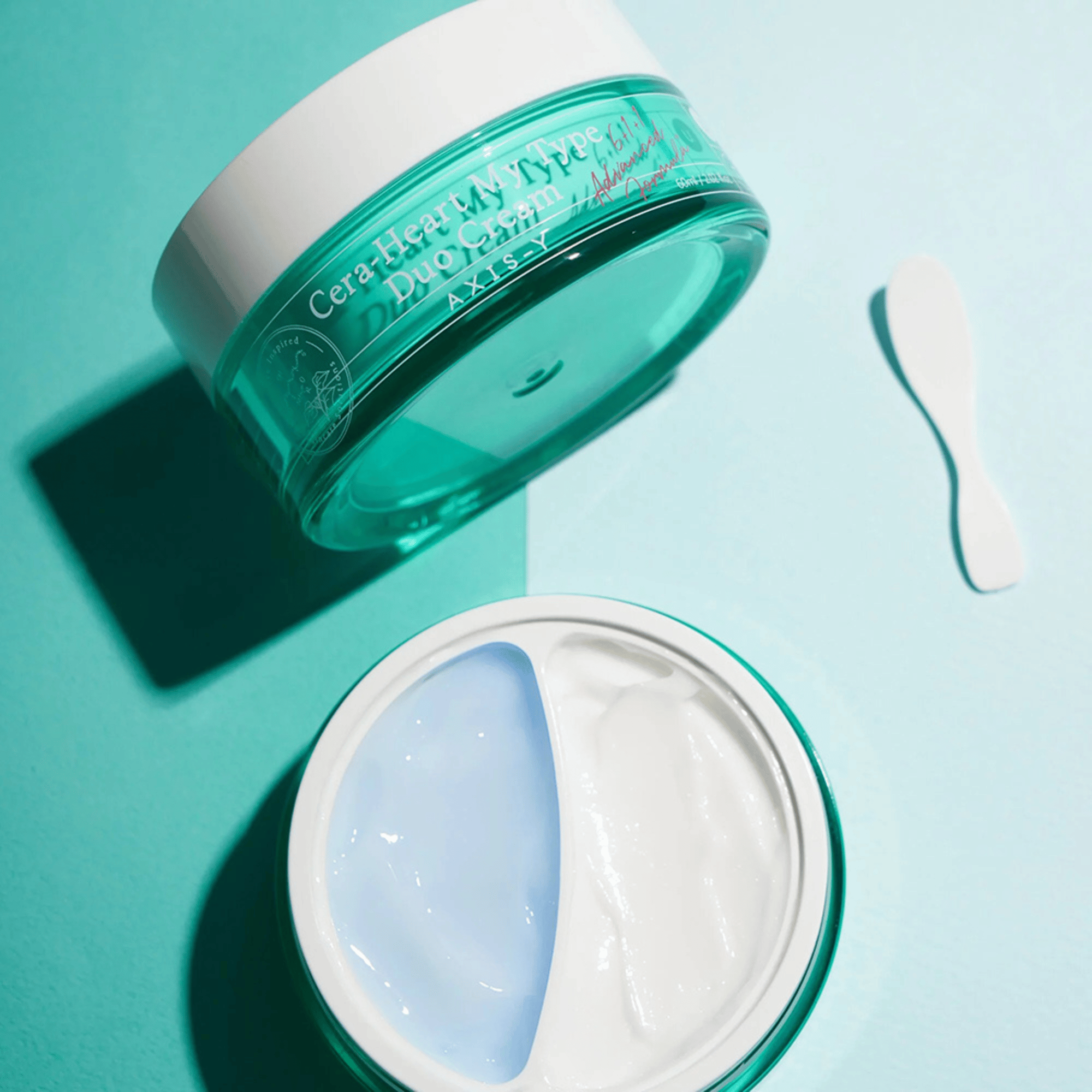 Geöffneter Tiegel der AXIS-Y Cera-Heart My Type Duo Cream mit blauer und weißer Textur auf türkisem Untergrund