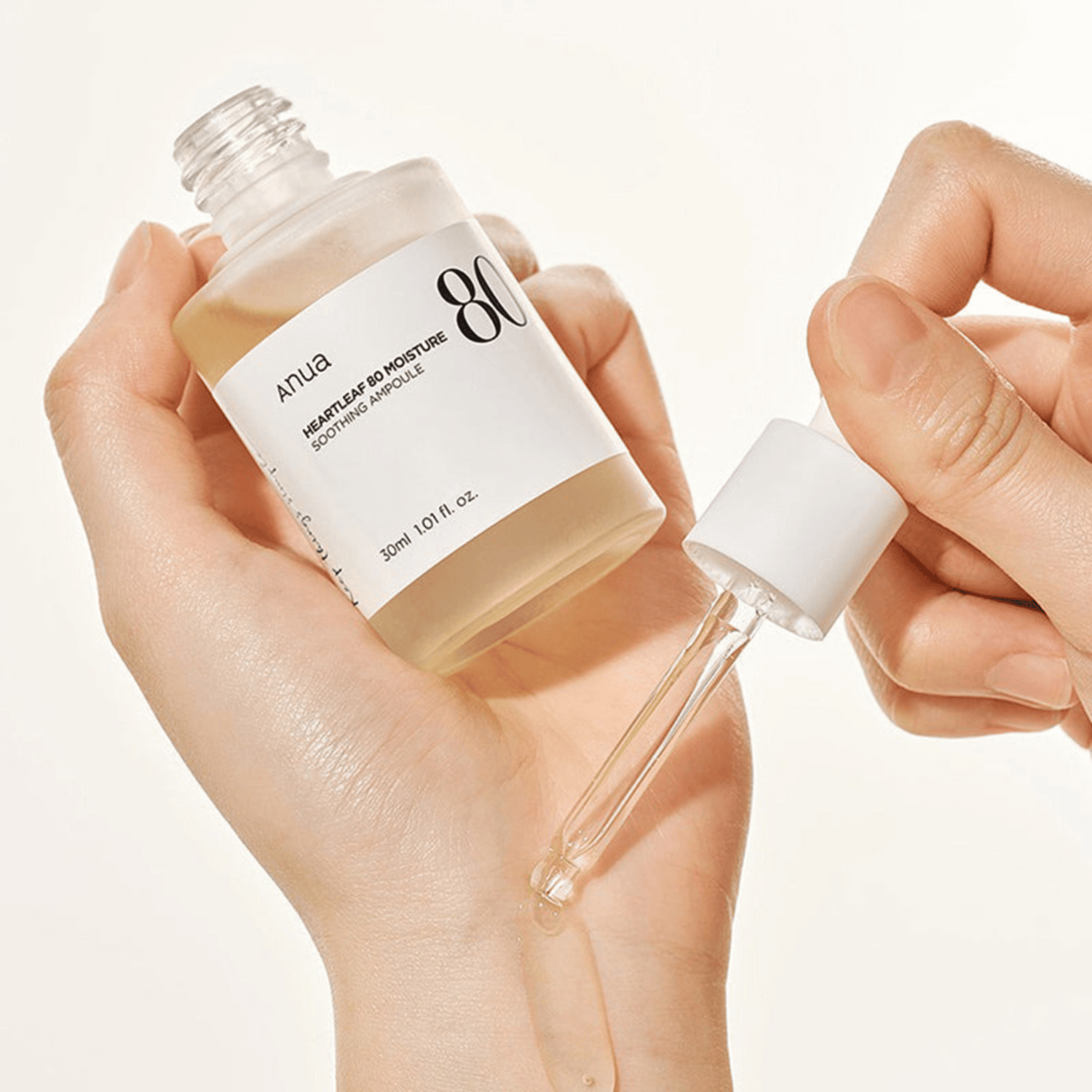 Eine Hand hält eine geöffnete Flasche Anua Heartleaf 80% Soothing Ampoule 30ml, während eine Pipette die Flüssigkeit auf den Rücken einer anderen Hand tropft.