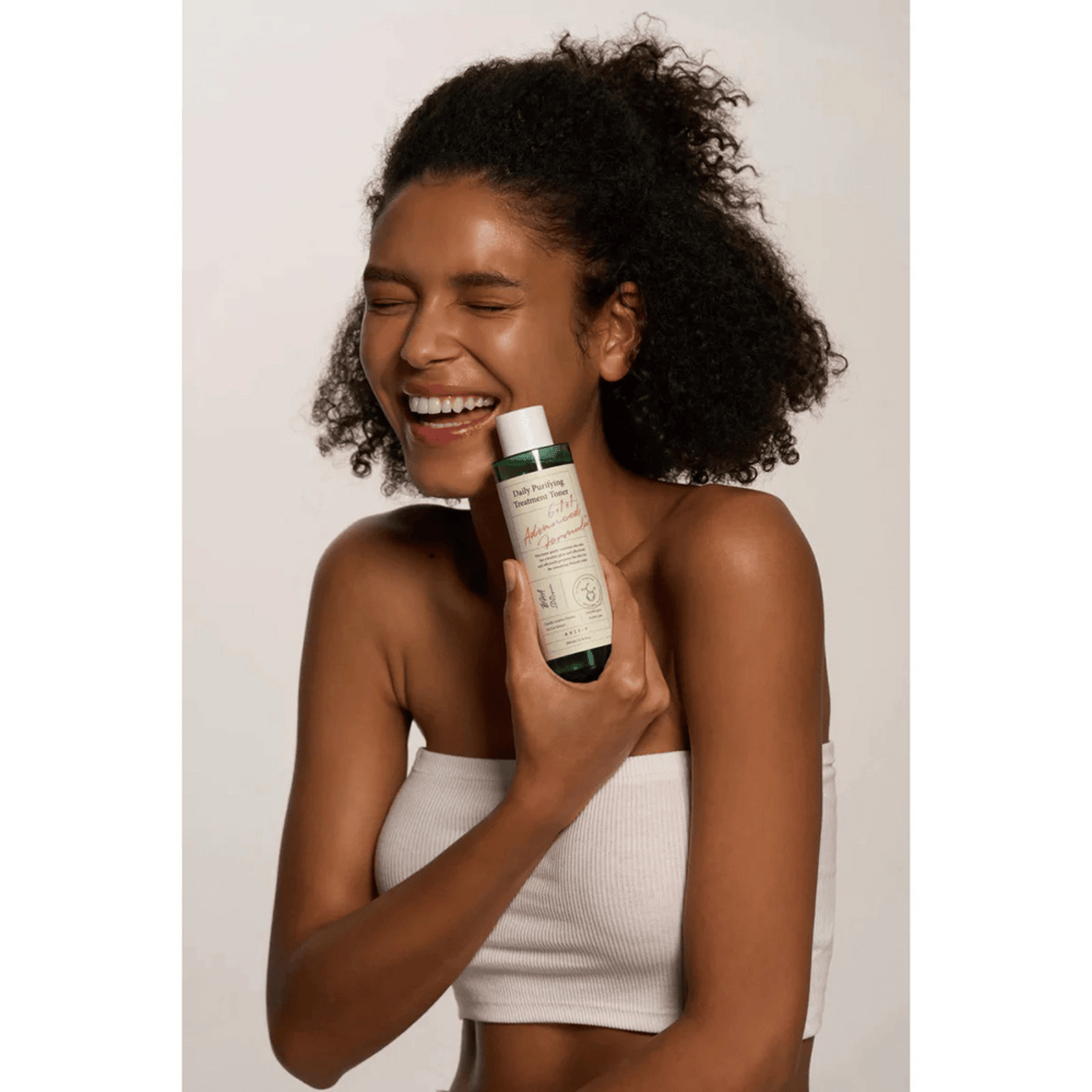 Lächelnde Frau hält den Axis-Y Daily Purifying Treatment Toner in der Hand und posiert mit geschlossenen Augen