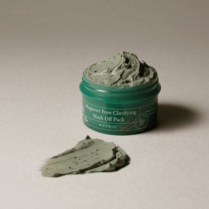 Axis-Y Mugwort Pore Clarifying Wash Off Pack mit einem geöffneten Tiegel, daneben eine cremige Portion auf hellem Hintergrund