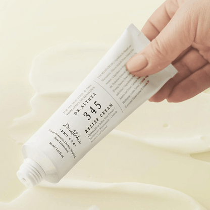 Eine Hand hält eine Tube Dr. Althea 345 Relief Cream mit veganer Formel vor einem cremigen, hellen Hintergrund.