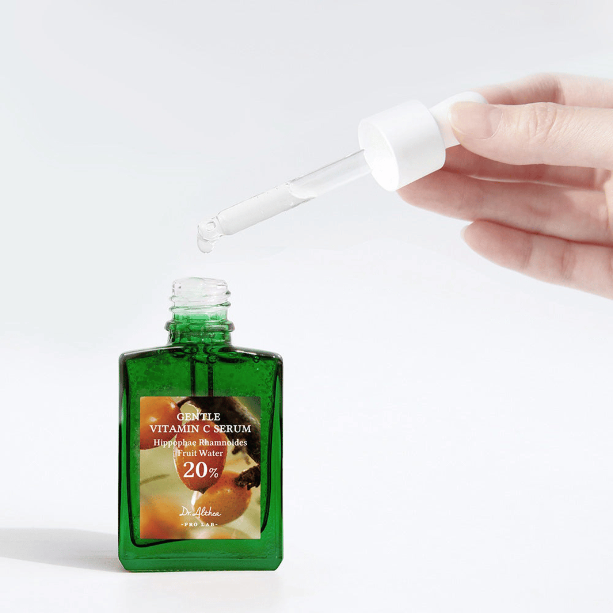 Eine Hand dosiert eine Pipette über eine grüne Glasflasche auf leicht grauen Hintergund.