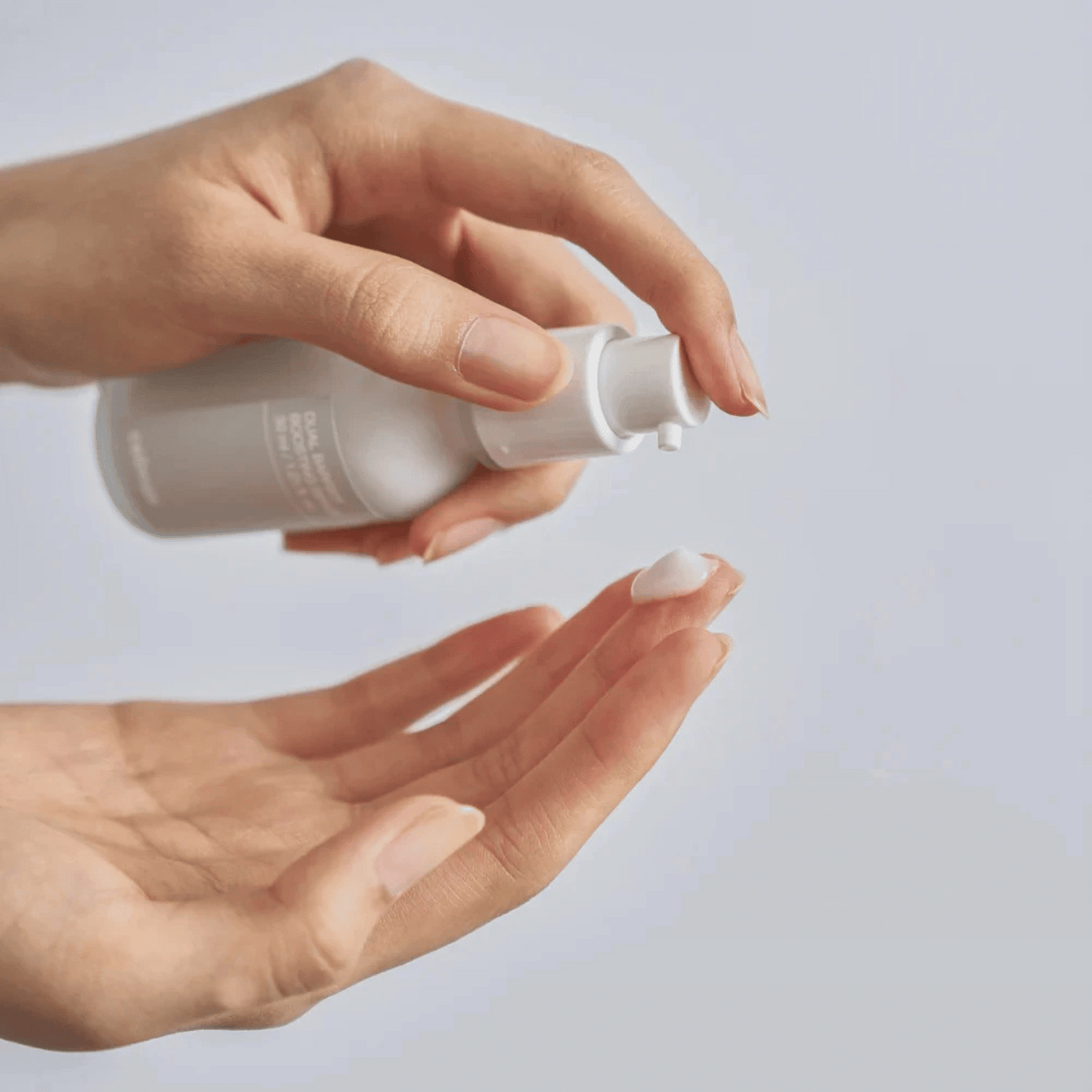 Eine Person verteilt eine kleine Menge des Celimax Dual Barrier Boosting Serum 30ml, einer weißen Lotion, aus der Pumpflasche auf ihre Fingerspitze vor einem unifarbenen Hintergrund.