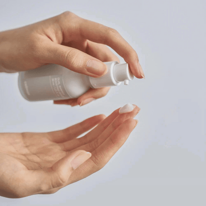 Eine Person verteilt eine kleine Menge des Celimax Dual Barrier Boosting Serum 30ml, einer weißen Lotion, aus der Pumpflasche auf ihre Fingerspitze vor einem unifarbenen Hintergrund.