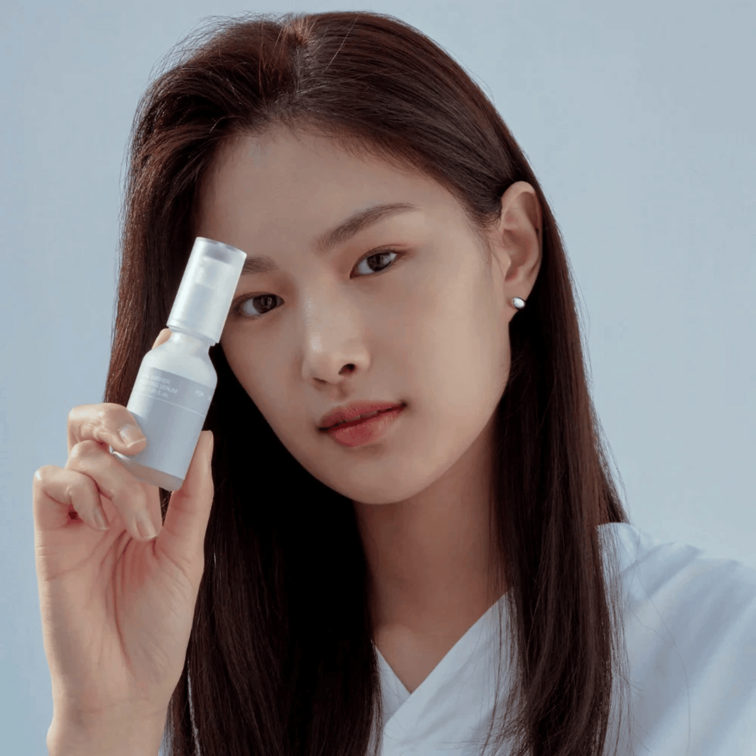 Eine Frau mit glattem dunklem Haar hält eine 30-ml-Flasche Celimax Dual Barrier Boosting Serum dicht vor ihr Gesicht und blickt in die Kamera vor einem schlichten hellblauen Hintergrund.