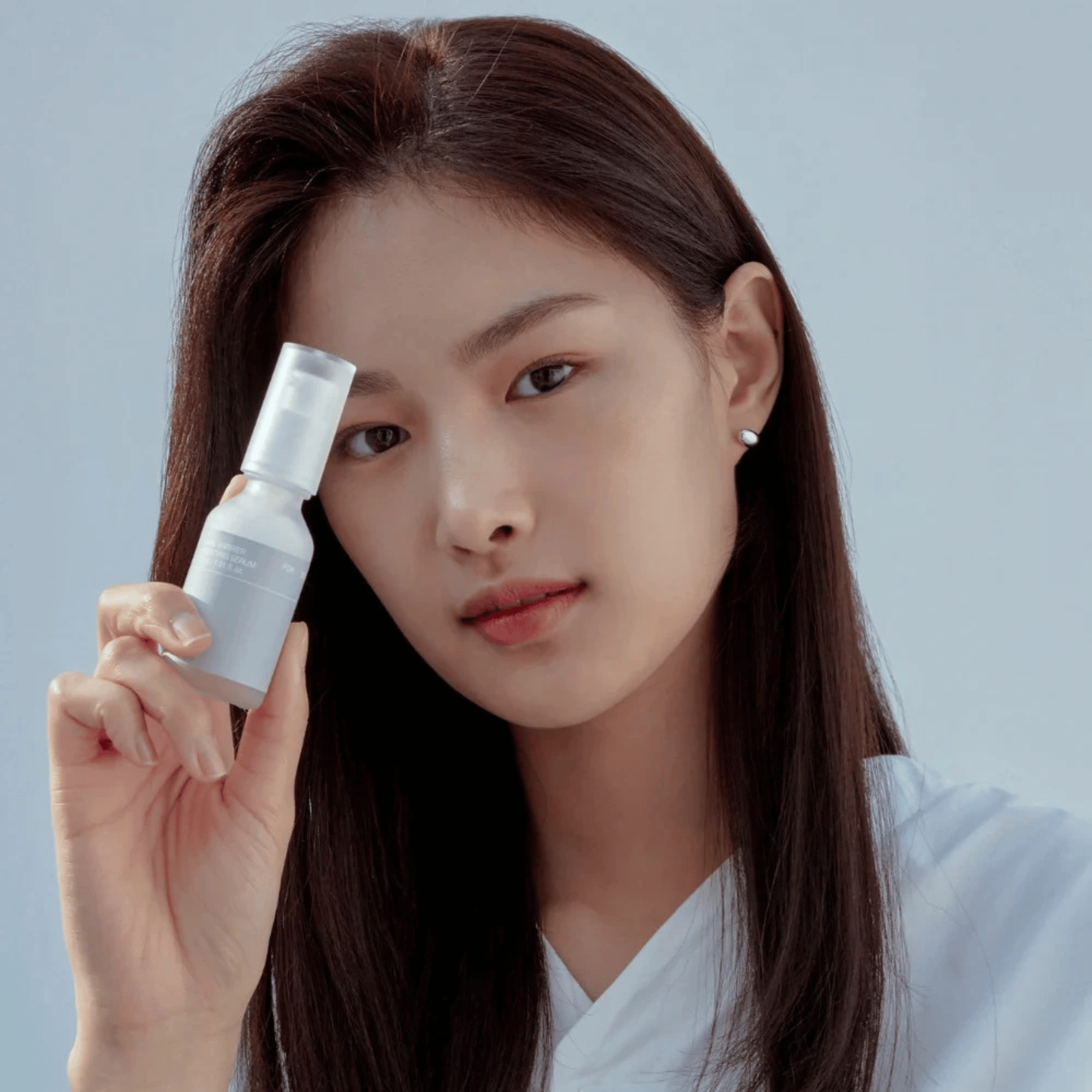 Eine Frau mit glattem dunklem Haar hält eine 30-ml-Flasche Celimax Dual Barrier Boosting Serum dicht vor ihr Gesicht und blickt in die Kamera vor einem schlichten hellblauen Hintergrund.