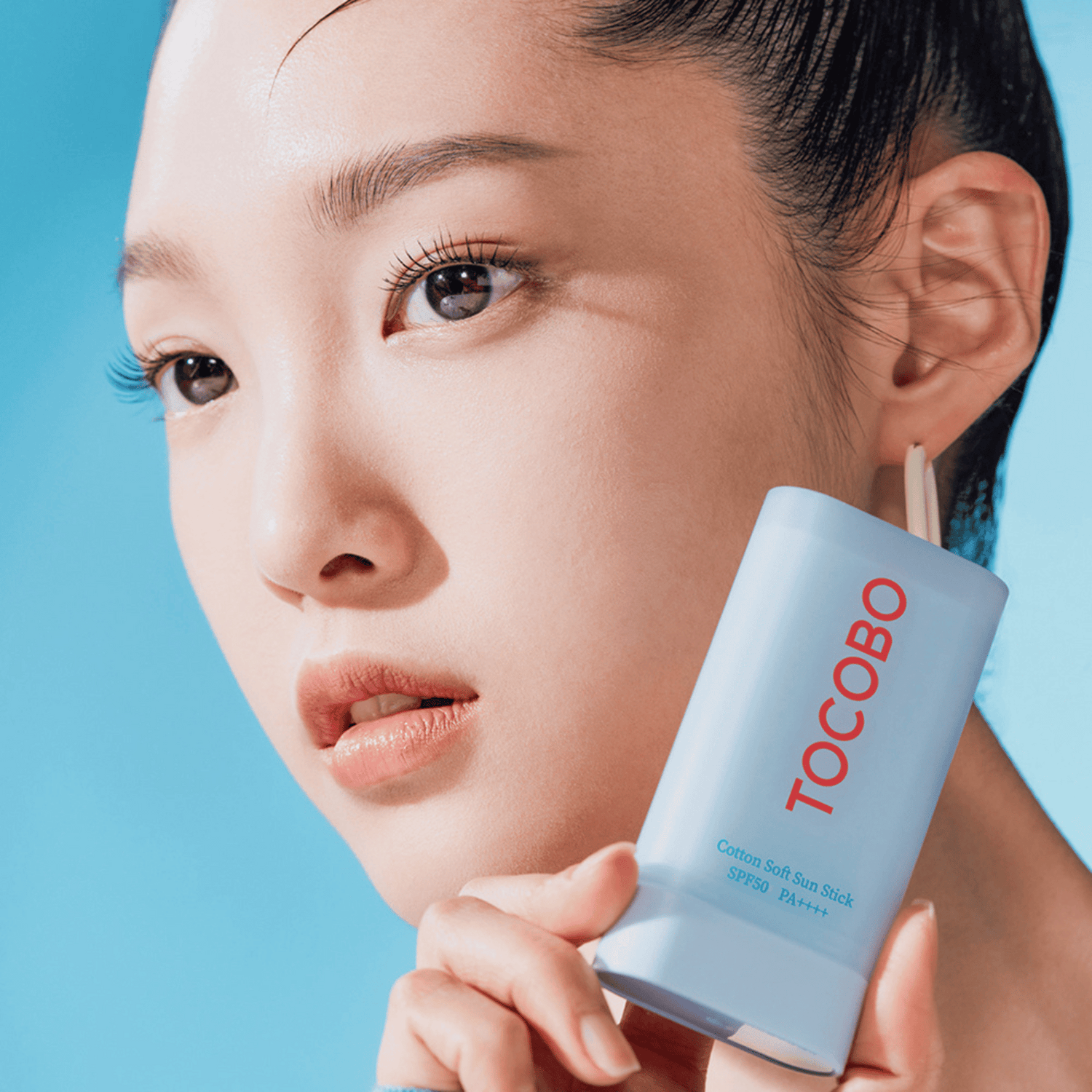 Nahaufnahme einer Frau mit makelloser Haut, die den hellblauen Tocobo Sonnenstick neben ihrem Gesicht präsentiert