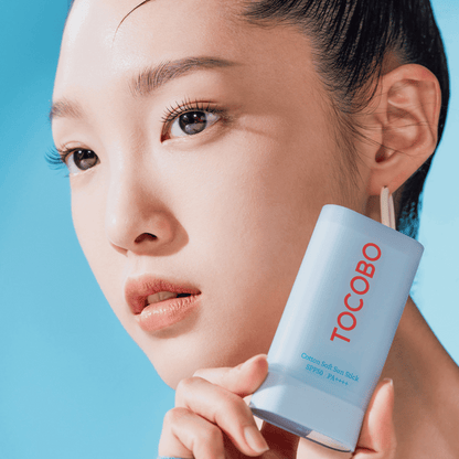 Nahaufnahme einer Frau mit makelloser Haut, die den hellblauen Tocobo Sonnenstick neben ihrem Gesicht präsentiert