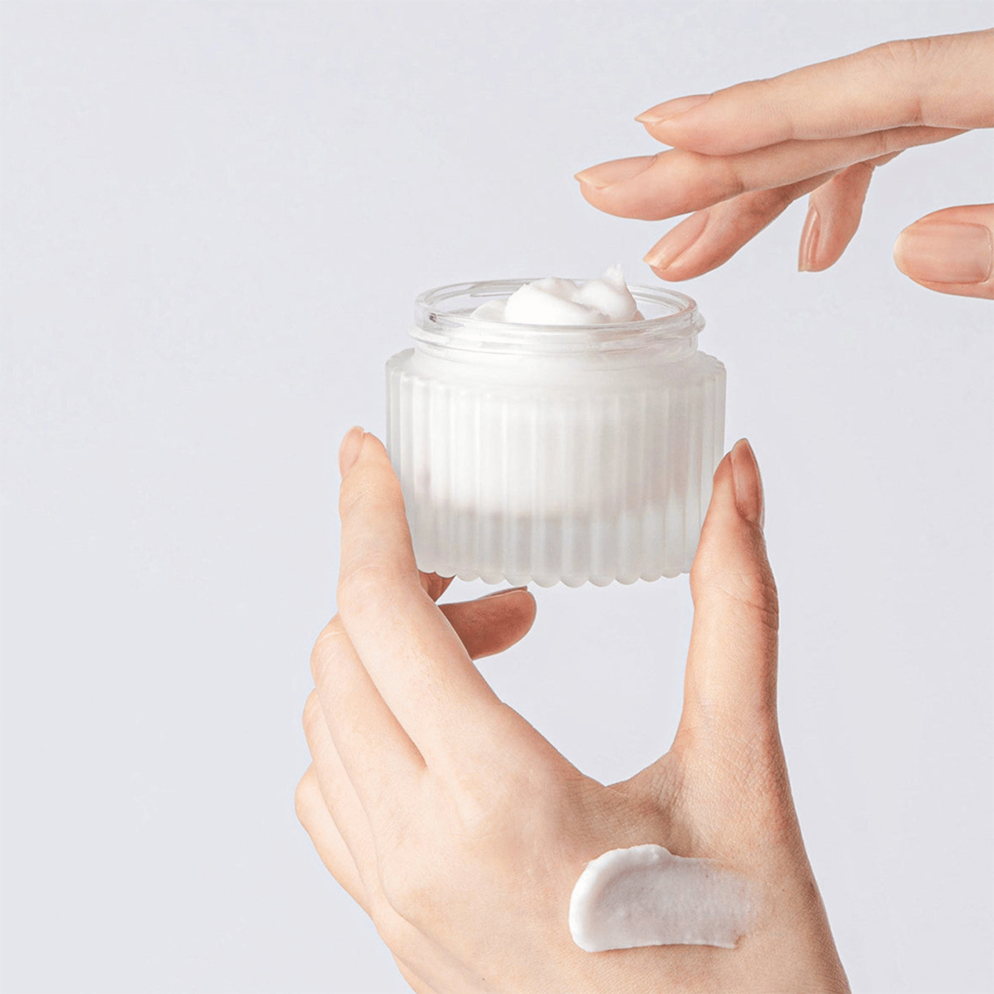 Hand trägt Tocobo Multi Ceramide Cream aus dem offenen Glasbehälter auf die Haut auf cremige Textur sichtbar