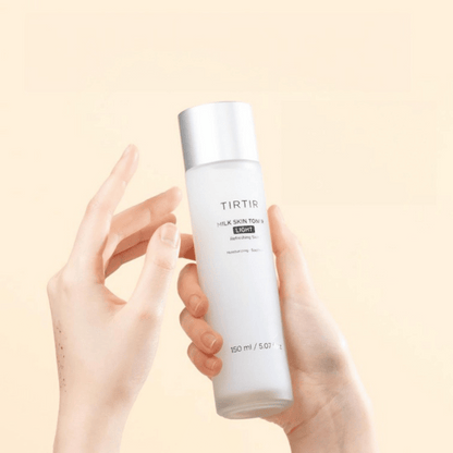 Zwei Hände halten die minimalistische Flasche des TIRTIR Milk Skin Toner Light 150ml vor pastellfarbenem Hintergrund