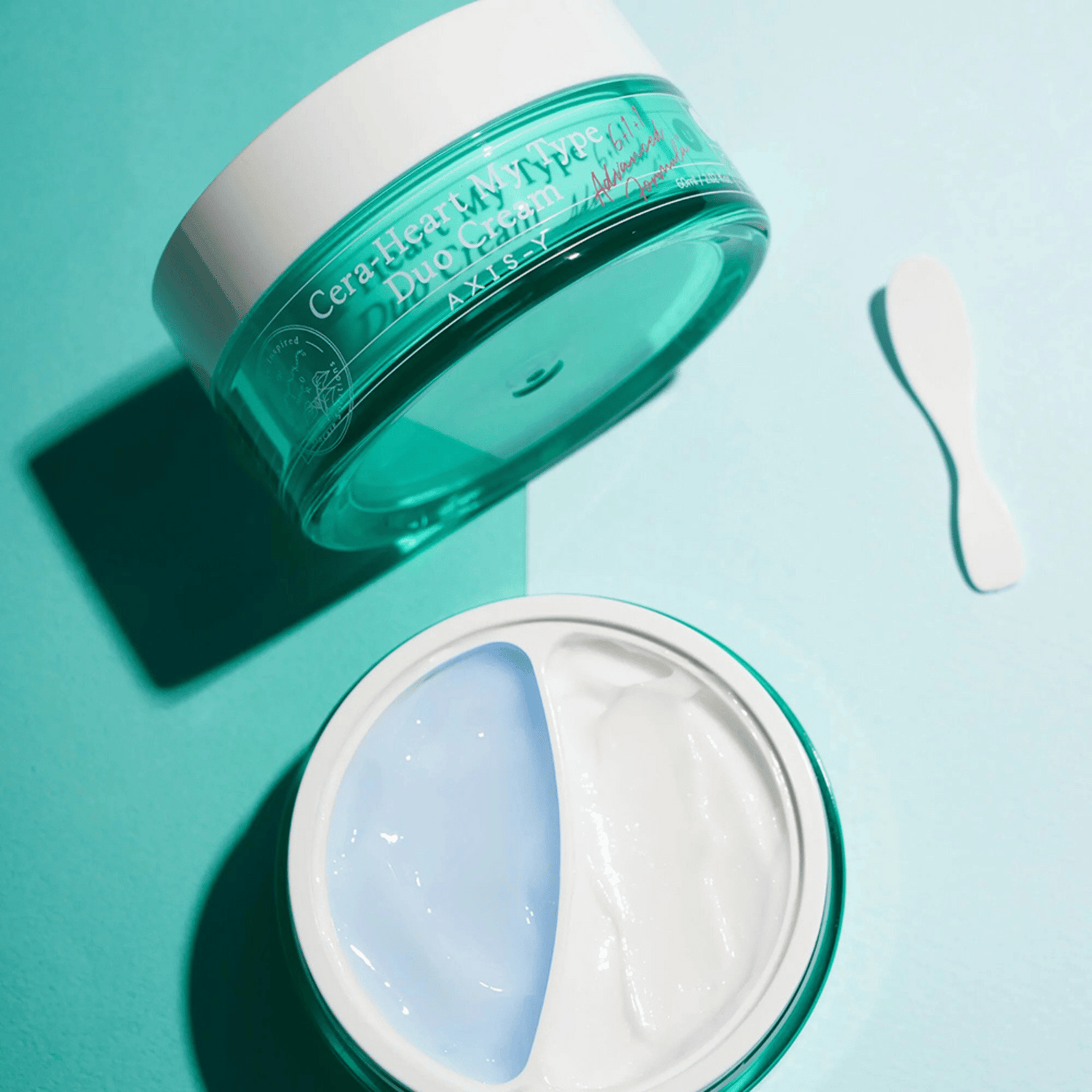 Geöffneter Tiegel der AXIS-Y Cera-Heart My Type Duo Cream mit blauer und weißer Textur auf türkisem Untergrund