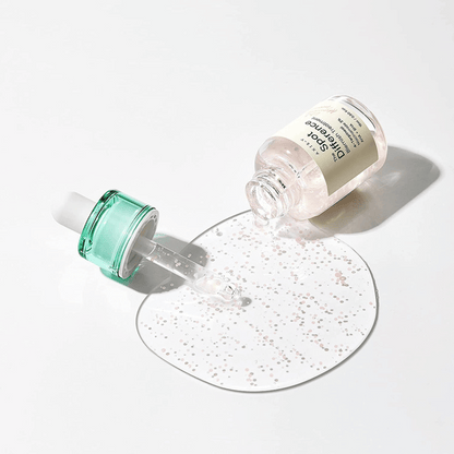 Offene Flasche des AXIS-Y Spot The Difference Blemish Treatment, daneben die Pipette mit transparenter Geltextur und pinken Perlen auf weißem Untergrund