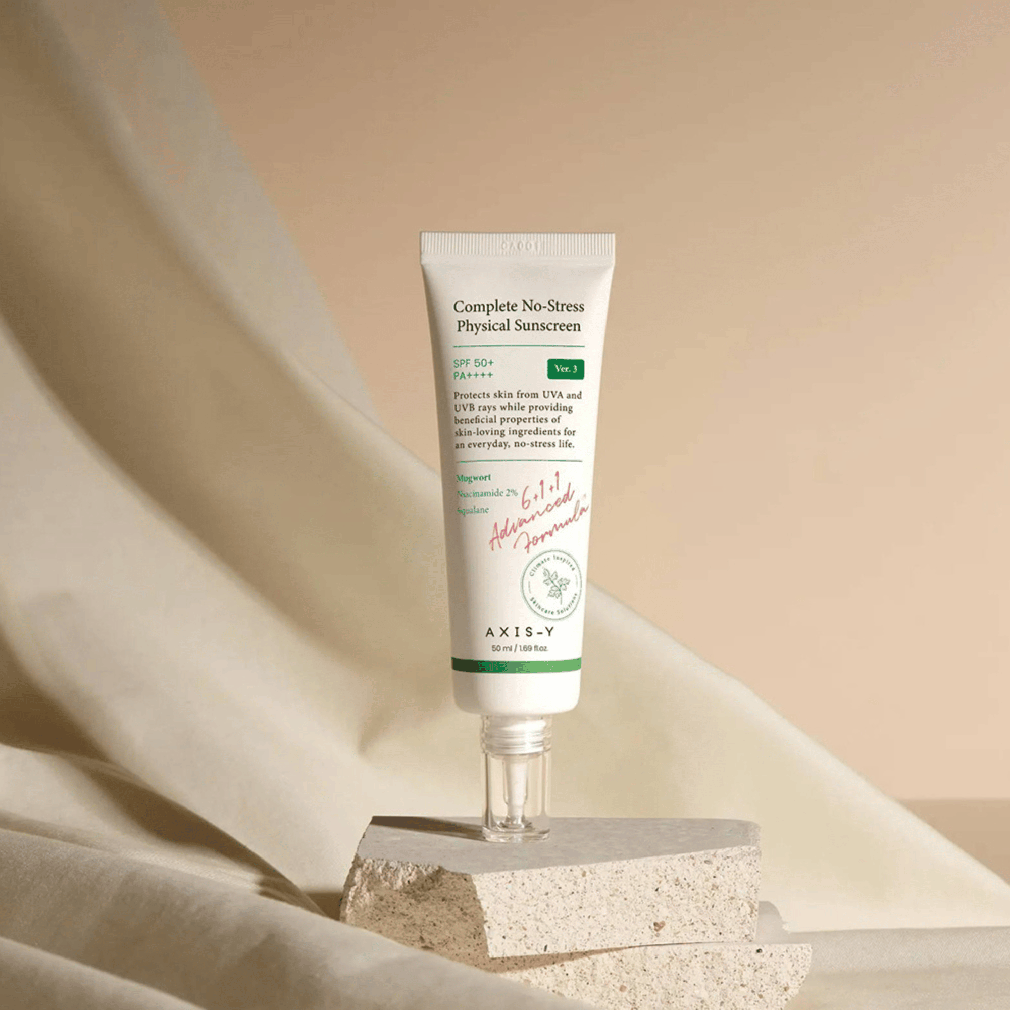 AXIS-Y Complete No-Stress Physical Sunscreen mit SPF 50+ auf strukturiertem Untergrund vor beigem Stoff im Hintergrund