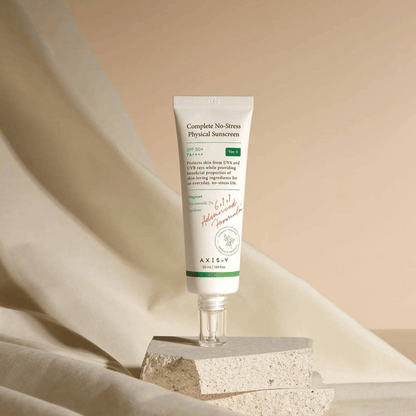AXIS-Y Complete No-Stress Physical Sunscreen mit SPF 50+ auf strukturiertem Untergrund vor beigem Stoff im Hintergrund