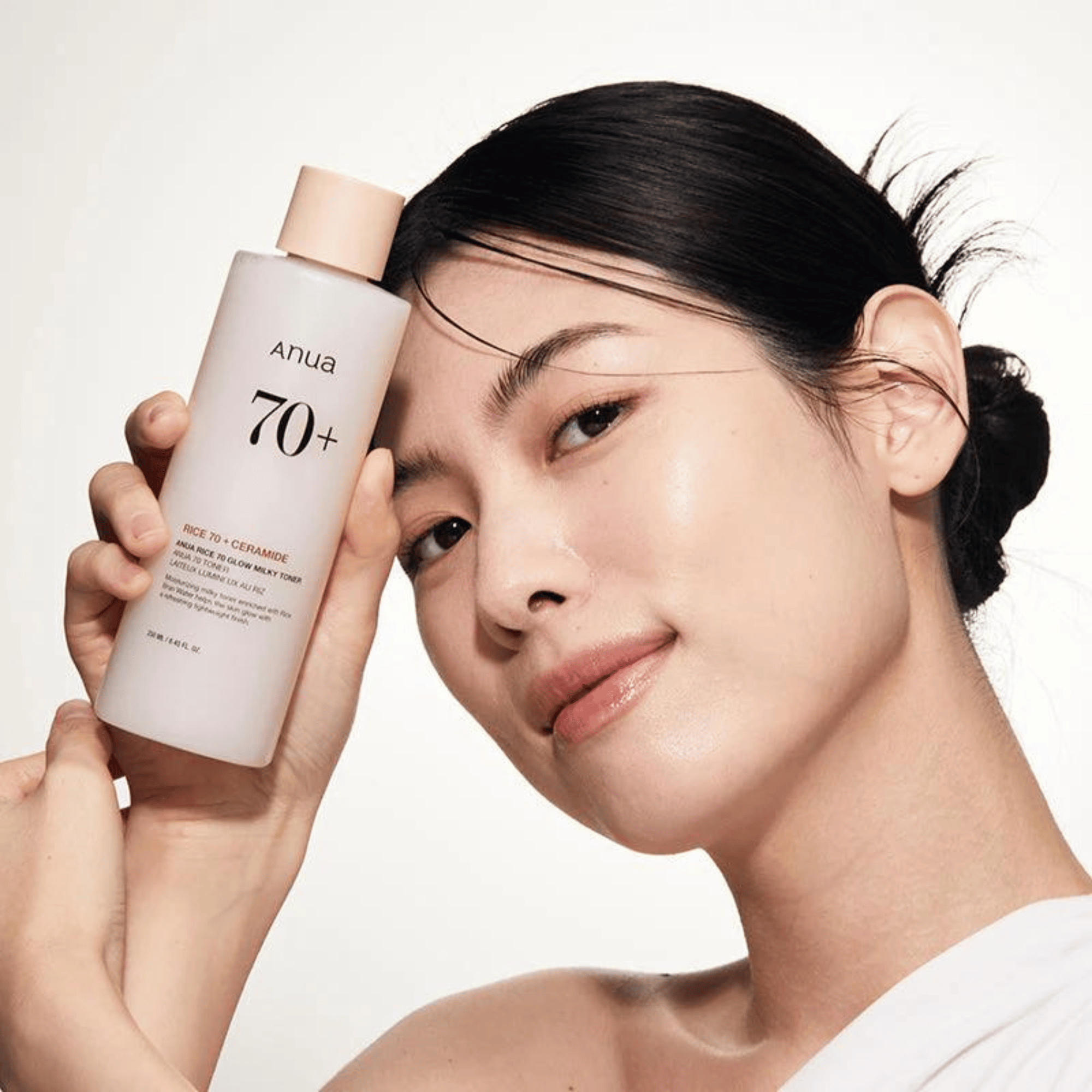 Modell mit strahlender Haut hält den Anua Rice 70+ Glow Milky Toner – ein Must-have in der korean skincare Routine