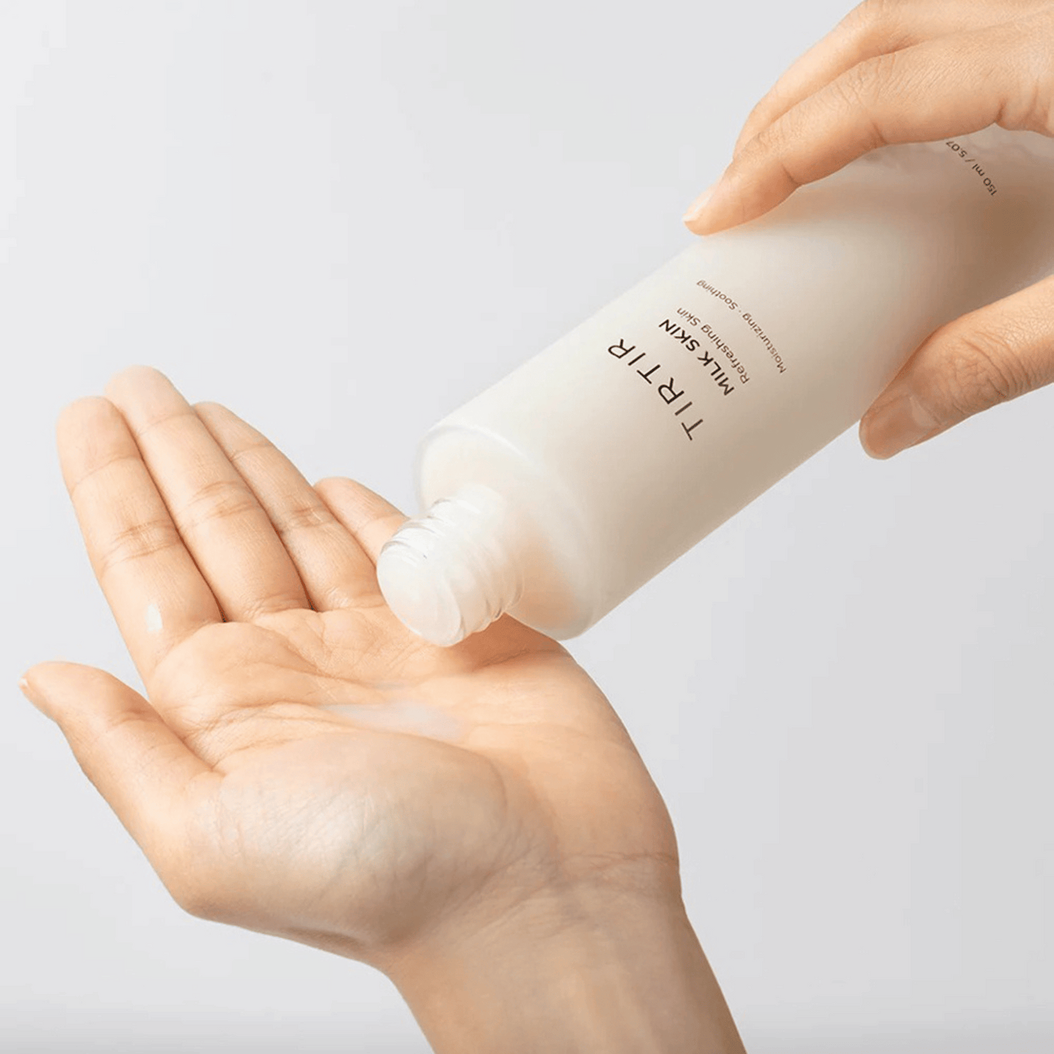 Zwei Hände halten die TIRTIR Milk Skin Toner Flasche vor beigem Hintergrund koreanische Hautpflege mit beruhigender Wirkung