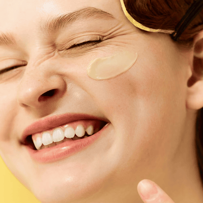 Eine Person lächelt mit geschlossenen Augen und trägt mit dem Finger Dr. Jart+ Ceramidin Skin Barrier Moisturizing Cream auf ihre Wange auf.